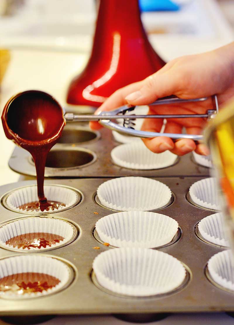 scooping batter into a c cupcake pan with liners in it.