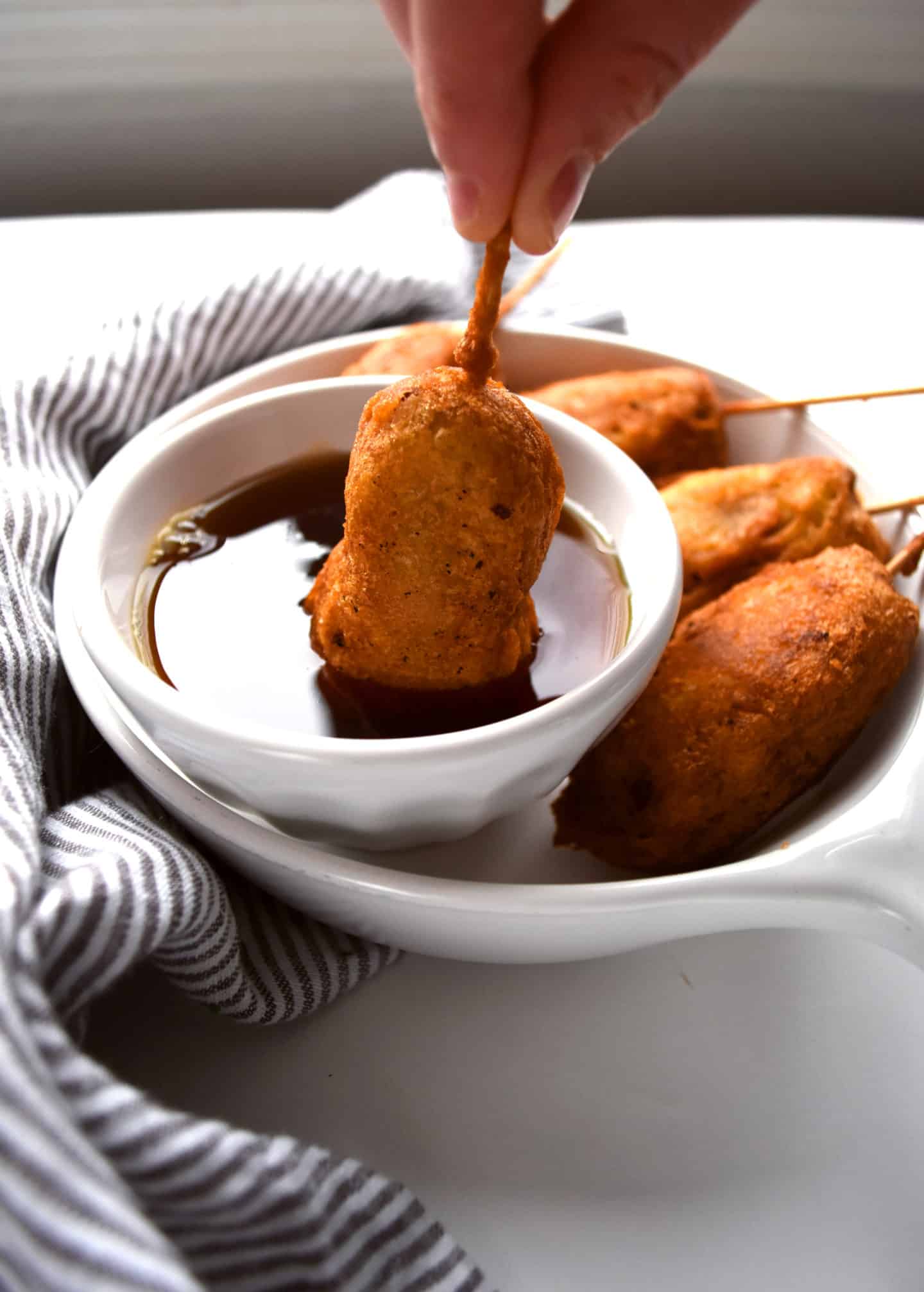 breakfast corn dogs being dipped into maple syrup