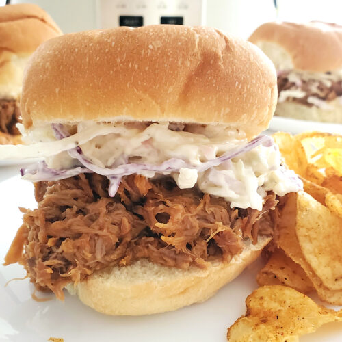 Shredded pork sandwich on a plated with a crockpot in the background