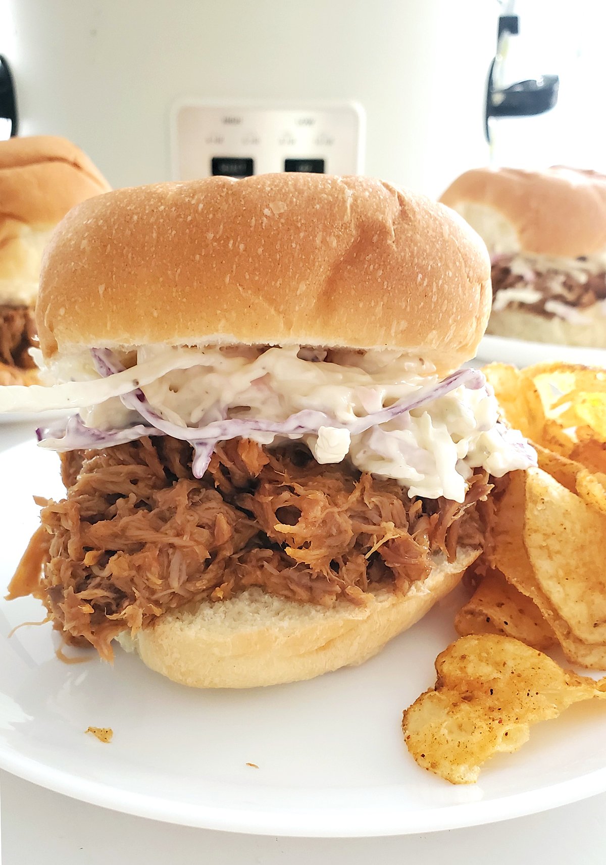 Shredded pork sandwich on a plated with a crockpot in the background